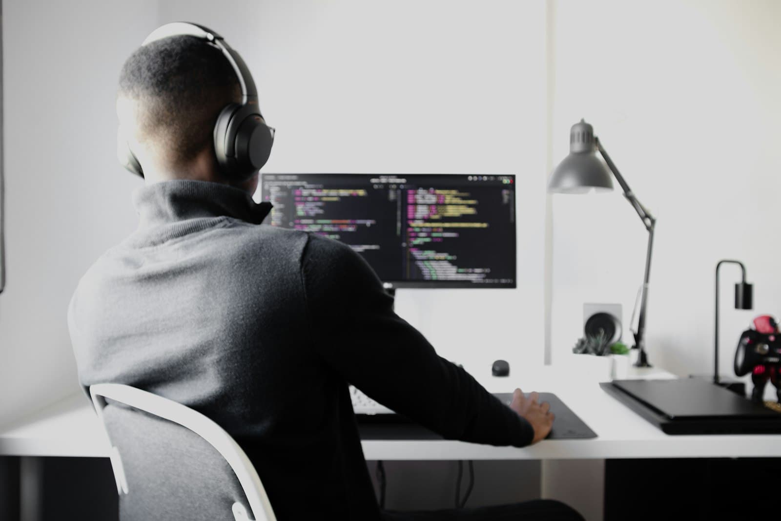 Chidi listening through headphones while working across two keyboards and a braille display.