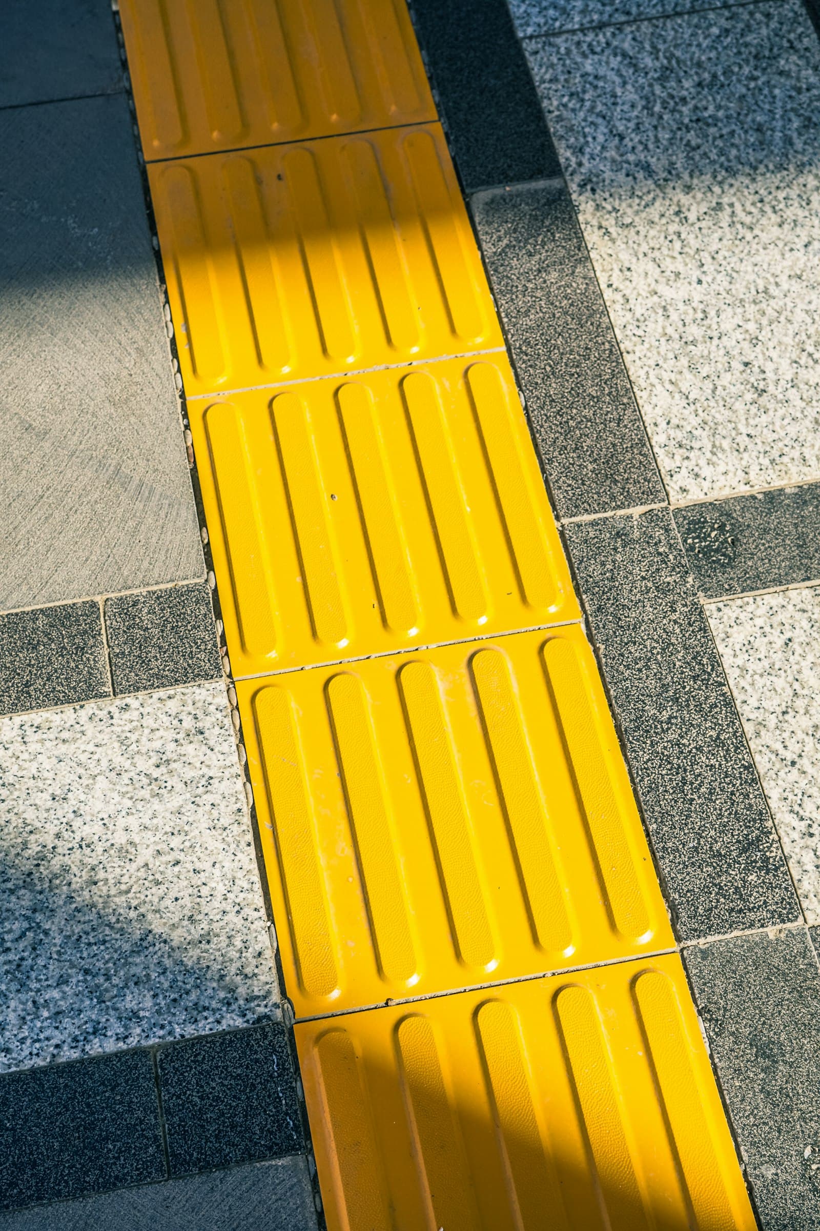 Bright yellow tactile paving guiding along a city footpath.